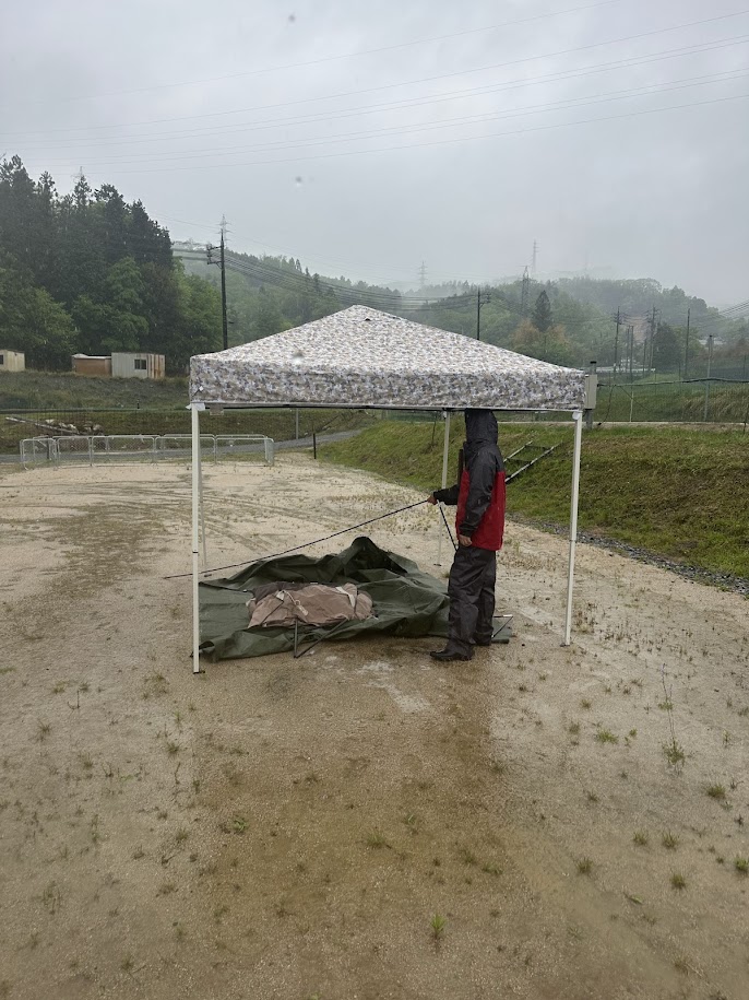 雨の中タープ下でテント設営中