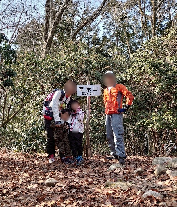 堂床山の山頂標識（標高859.6m）の前で記念撮影する家族4人