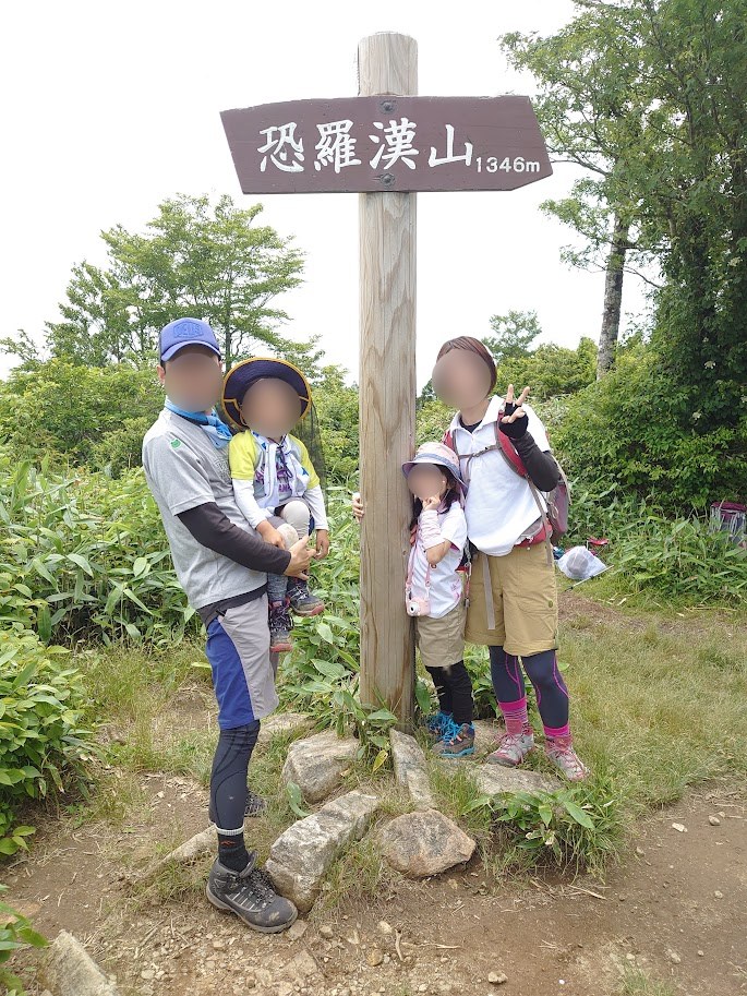 恐羅漢山の山頂標識（標高1346m）の前で記念撮影する家族4人