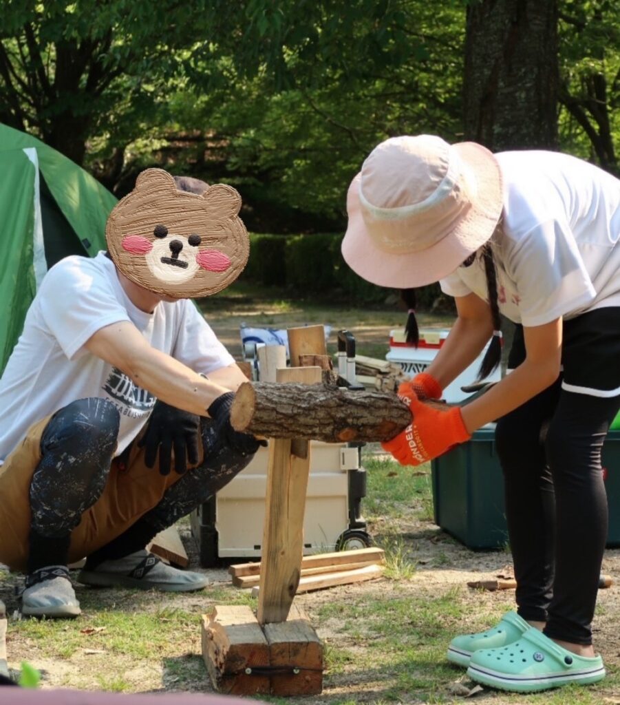 大人がナタを支え、子どもが薪で叩いて安全に薪割りをする様子