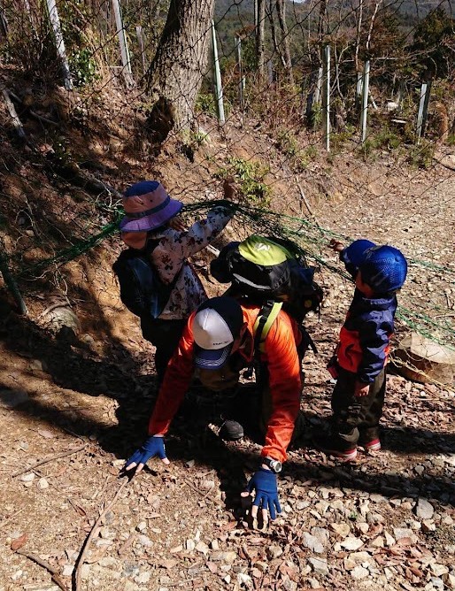 登山道に張られた獣よけネットの下をくぐって進む親子