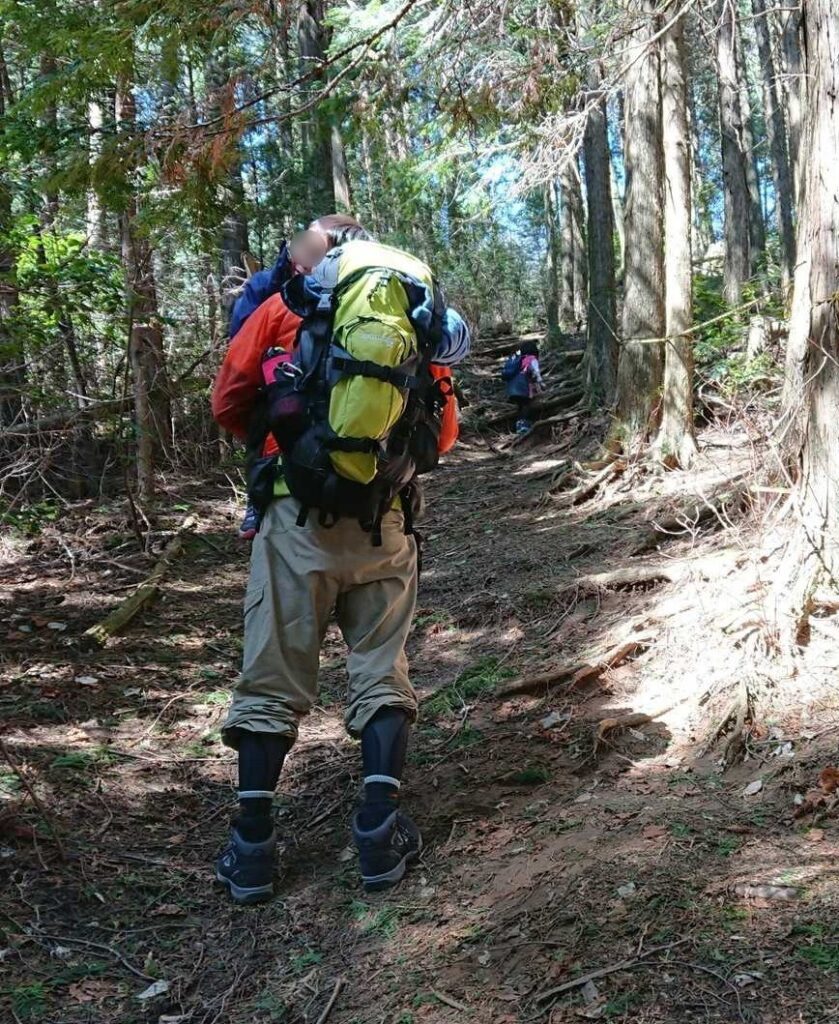 3歳の息子を抱っこして山頂手前の急な登りを進む後ろ姿。先を6歳の娘が歩く