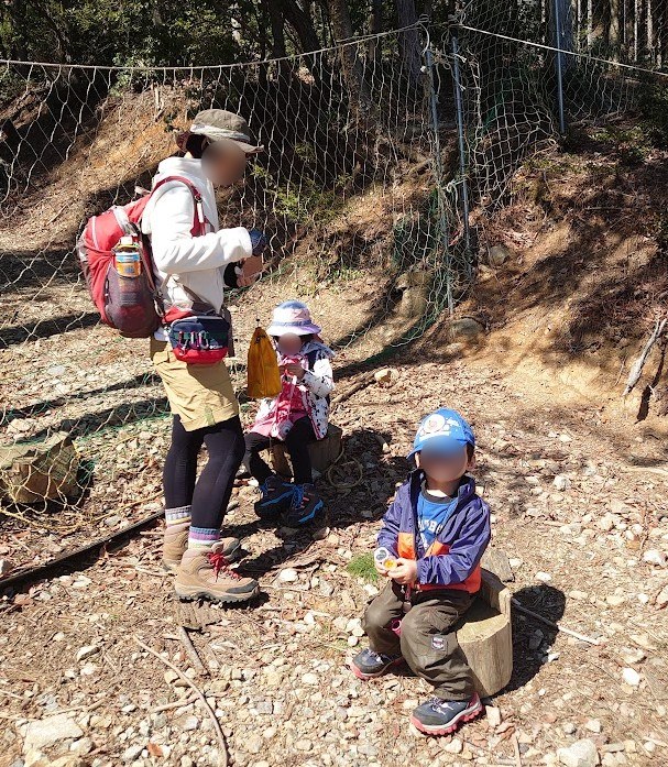 登山道脇の切り株に座っておやつを食べる6歳の娘と3歳の息子