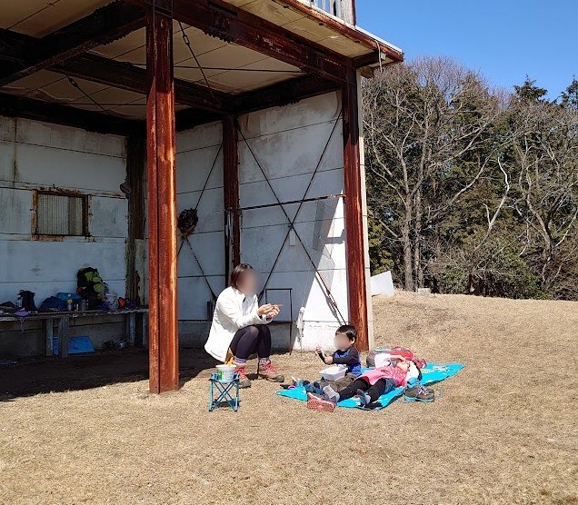 鷹ノ巣山山頂の休憩小屋のそばでレジャーシートを広げて休む親子