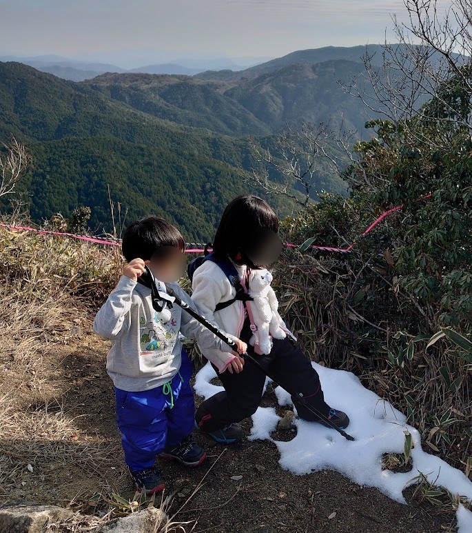可部冠山の山頂手前で、山並みを背にして残った雪をさわる6歳の娘と3歳の息子