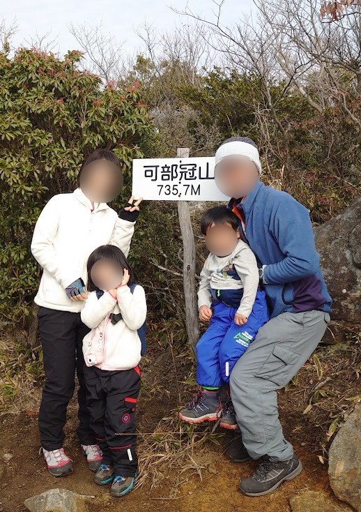 可部冠山の山頂標識（735.7m）の前で記念撮影する家族4人