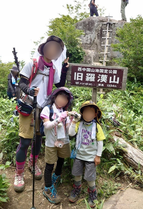 旧羅漢山の山頂標識(標高1334m)の前に立つ家族