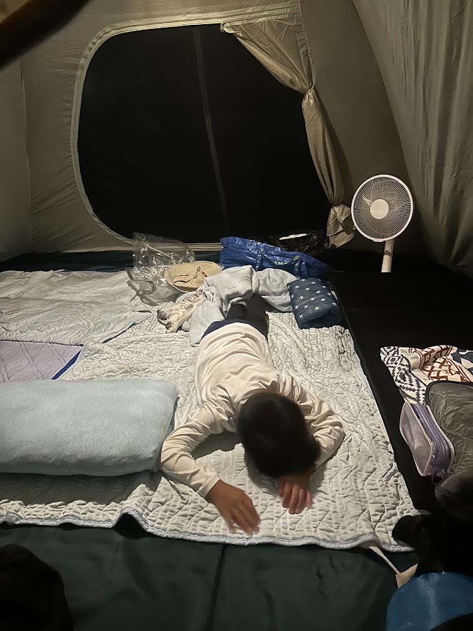 テント内で扇風機を回して眠る子ども