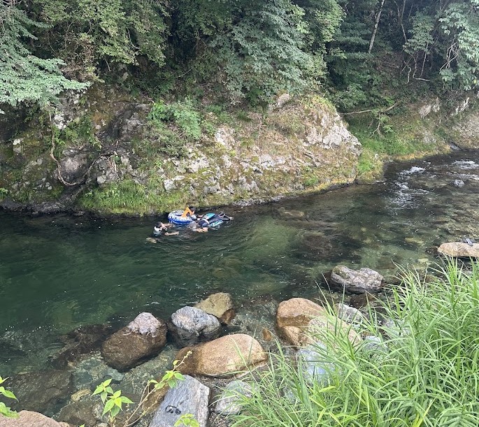 水深のある緑色の淵で浮き輪を使って泳ぐ人たち