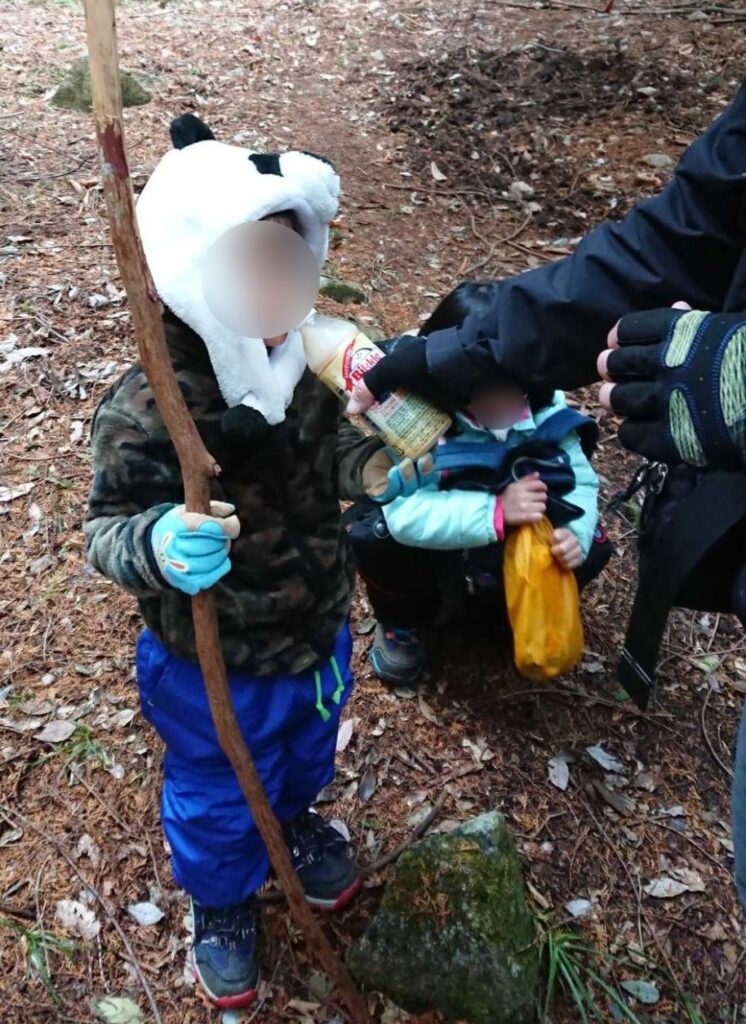 登山道で拾った枝を杖にして、おやつを受け取る3歳の息子と6歳の娘