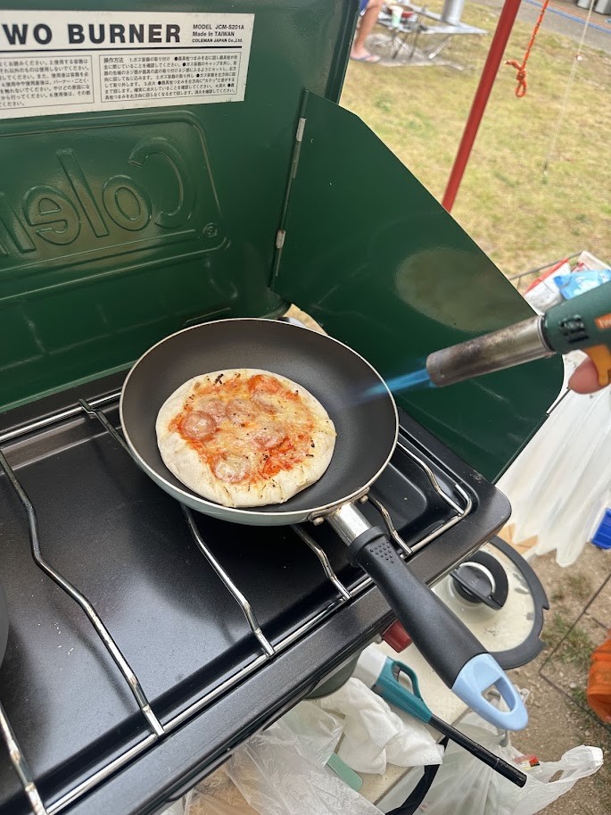 ツーバーナーの上のフライパンで焼いたピザをバーナーで炙る