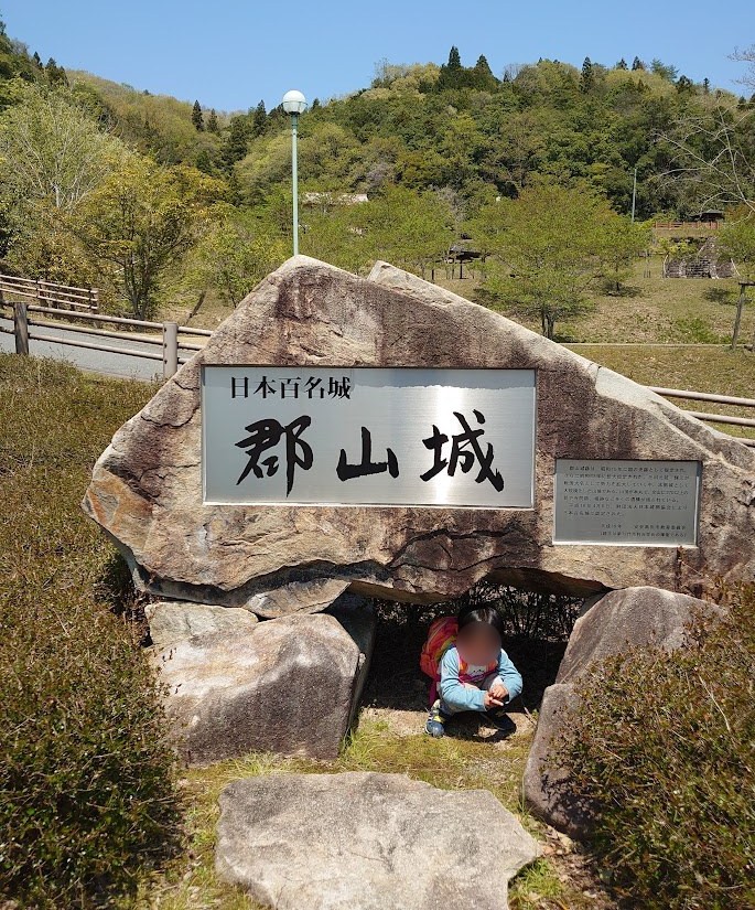 登山口近くに立つ「日本百名城 郡山城」と刻まれた石碑と、その下でしゃがむ子ども