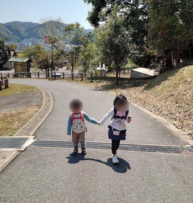 手をつないで舗装路を歩き出す姉弟の後ろ姿と、奥に見える吉田の町並み
