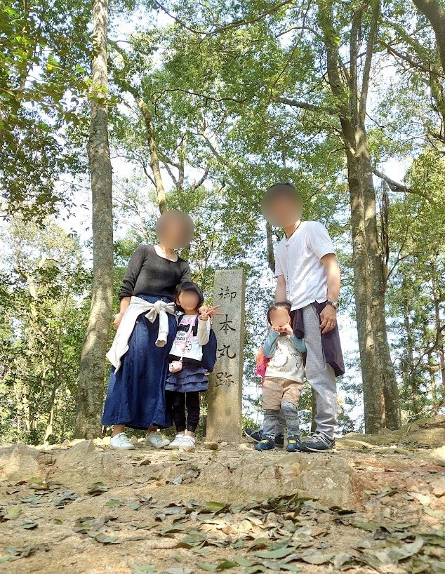 郡山城の本丸跡の石柱の前に並ぶ家族4人