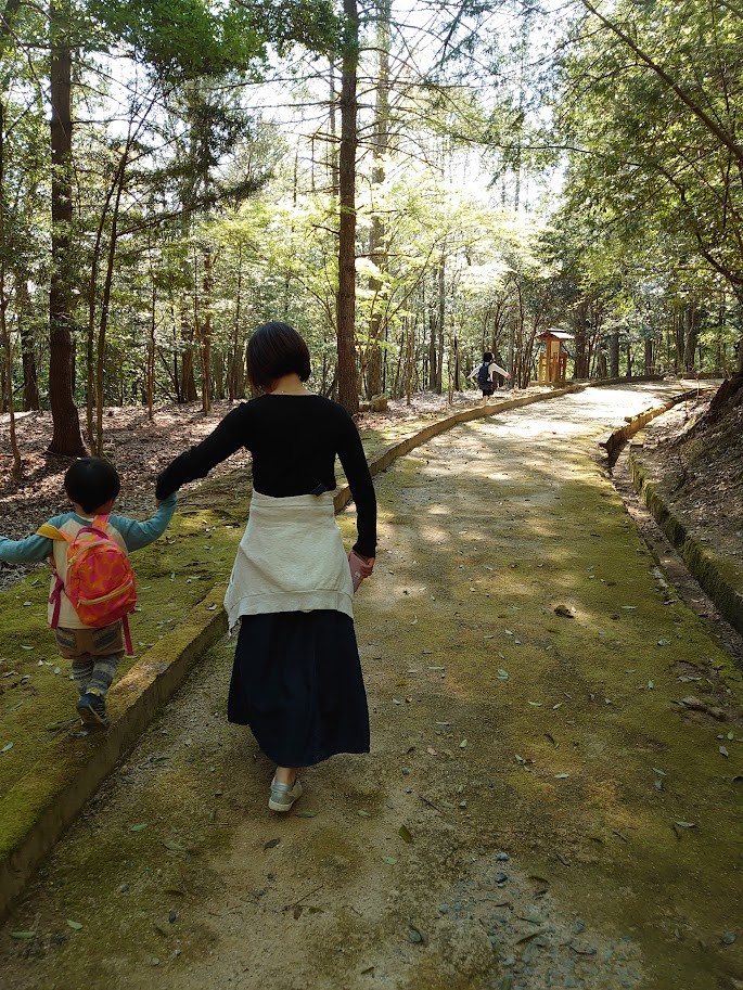 道幅の広い下山路を、手をつないで歩くママと息子の後ろ姿