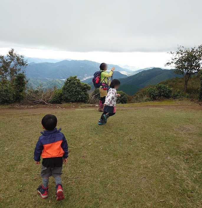 白木山の山頂の広場を歩く子どもたちと周りの山並み