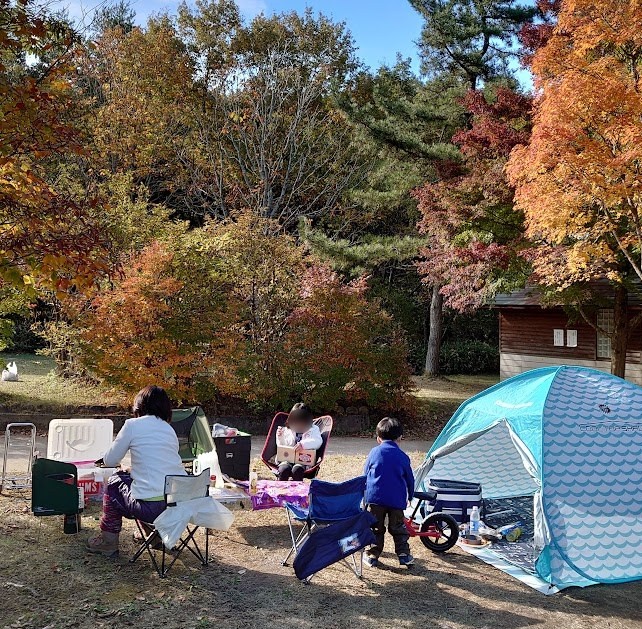 紅葉に囲まれた聖湖キャンプ場でデイキャンプランチをする家族とテント