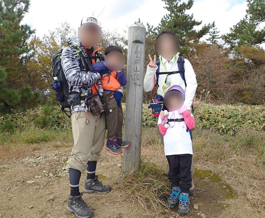 雲月山の山頂標識の前で記念撮影する家族4人