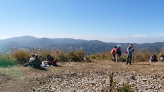 深入山の広い山頂でくつろぐ登山者たちと、遠くに広がる山並み