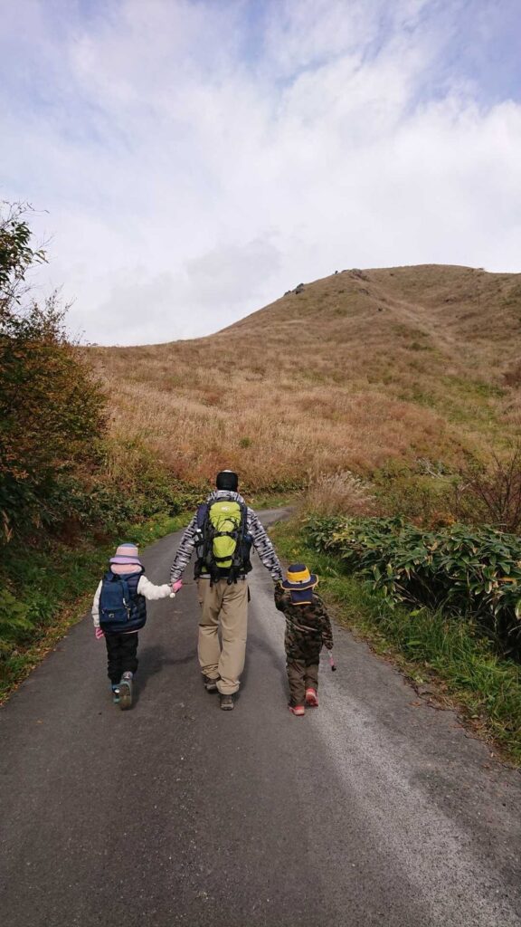 雲月峠へ続く車道を手をつないで歩く父と子ども2人の後ろ姿