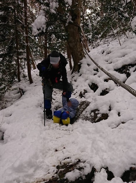 雪の下り坂で足を滑らせた息子と、そばで支える大人