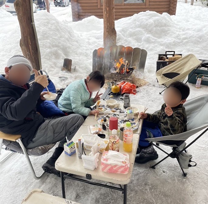 雪中キャンプで、ダウンを着てごはんを食べる家族