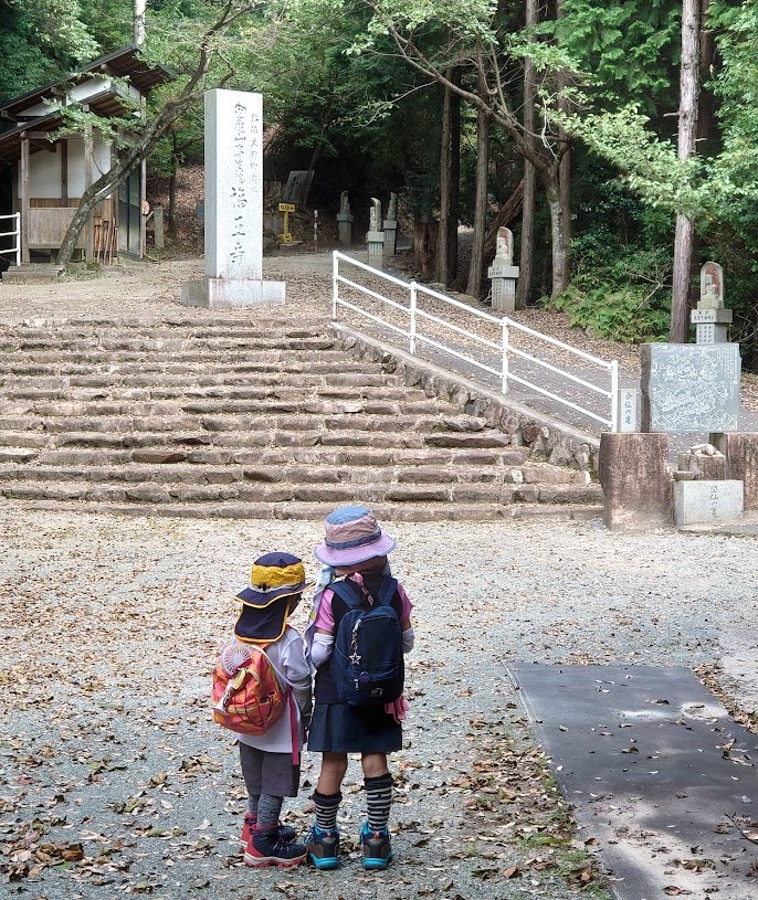 福王寺の石碑と石段の前に並ぶ子どもたちの後ろ姿