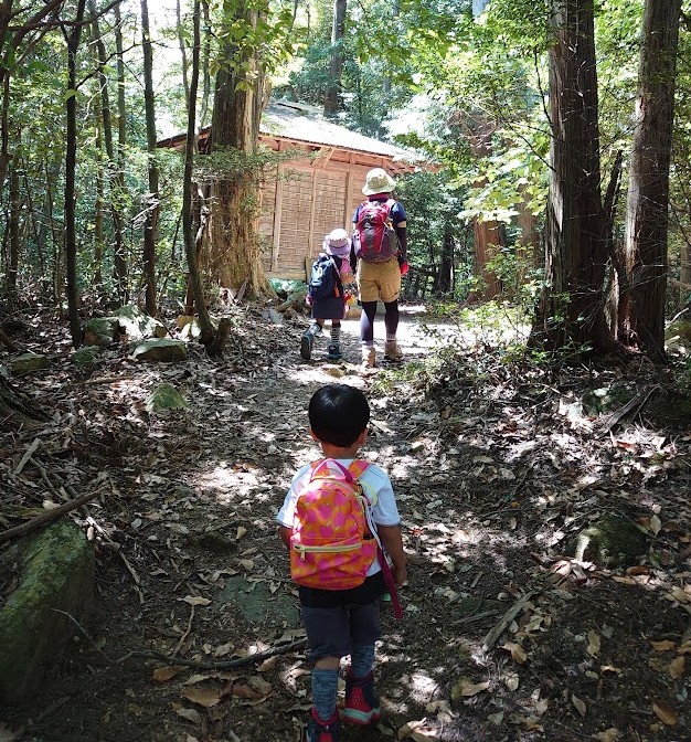 木漏れ日の登山道の先に見える三鬼堂と、歩く家族の後ろ姿