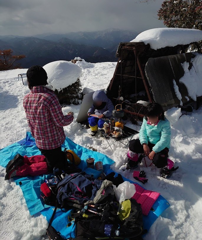牛頭山の山頂の雪の上でシートを広げてランチの準備をする家族