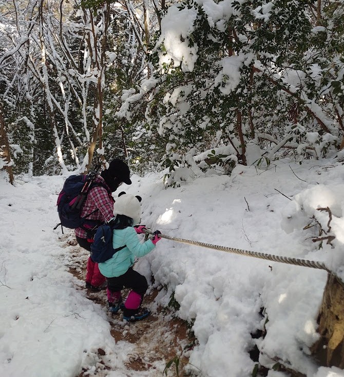 ロープをつかんで雪の登山道を登る親子