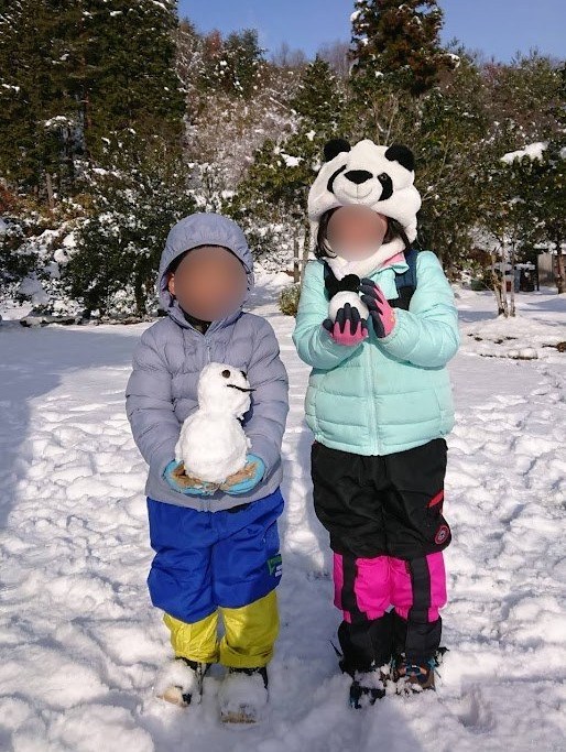 雪だるまを持つ子ども2人。ダウンとスノーパンツの冬の服装