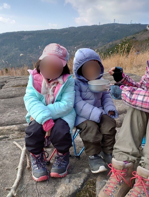 山でダウンを着てお昼ごはんを食べる子ども2人