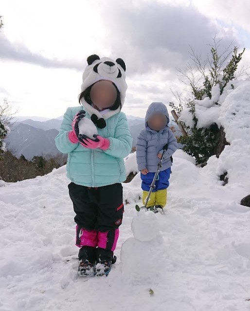 雪の上に立つ子ども2人。娘はピンク、息子は黄色のゲーターを付けている